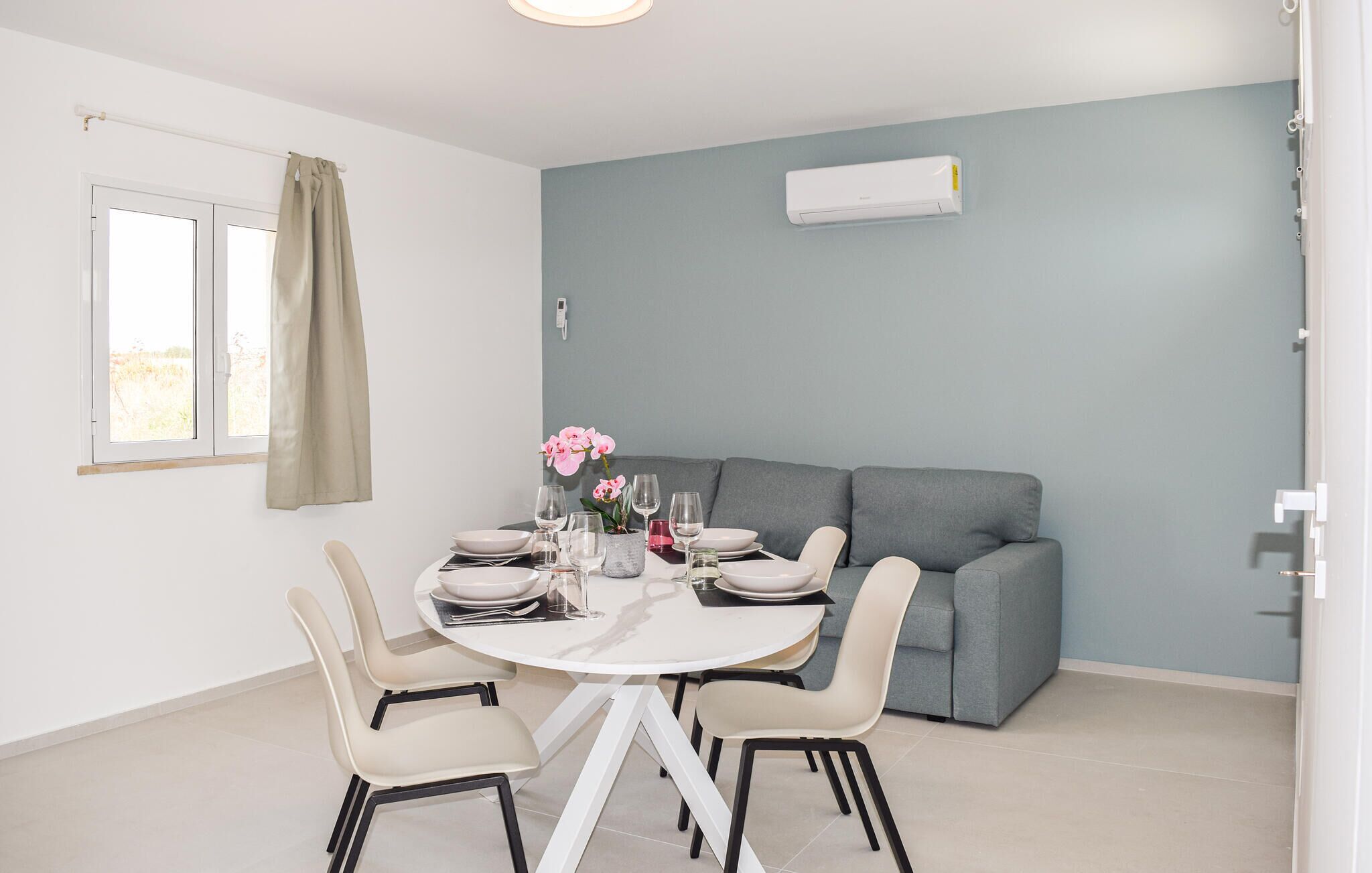 A modern dining area with a round table, white chairs, and a grey sofa.