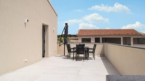 A rooftop terrace with a table and chairs, a covered area, and a building with a tiled roof in the background. - Nice home in Marina di Ragusa (Marina di Ragusa)