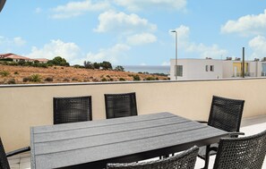 Eine Dachterrasse mit Tisch und Stühlen, mit Blick auf eine hügelige Landschaft und ein Gewässer.