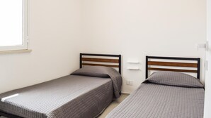 A small, single-room accommodation with two single beds, each with a wooden headboard and grey bedding. - Nice home in Marina di Ragusa (Marina di Ragusa)