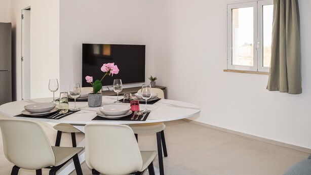 A dining area with a round table set for two, a television, and a window with curtains. - Nice home in Marina di Ragusa (Marina di Ragusa)