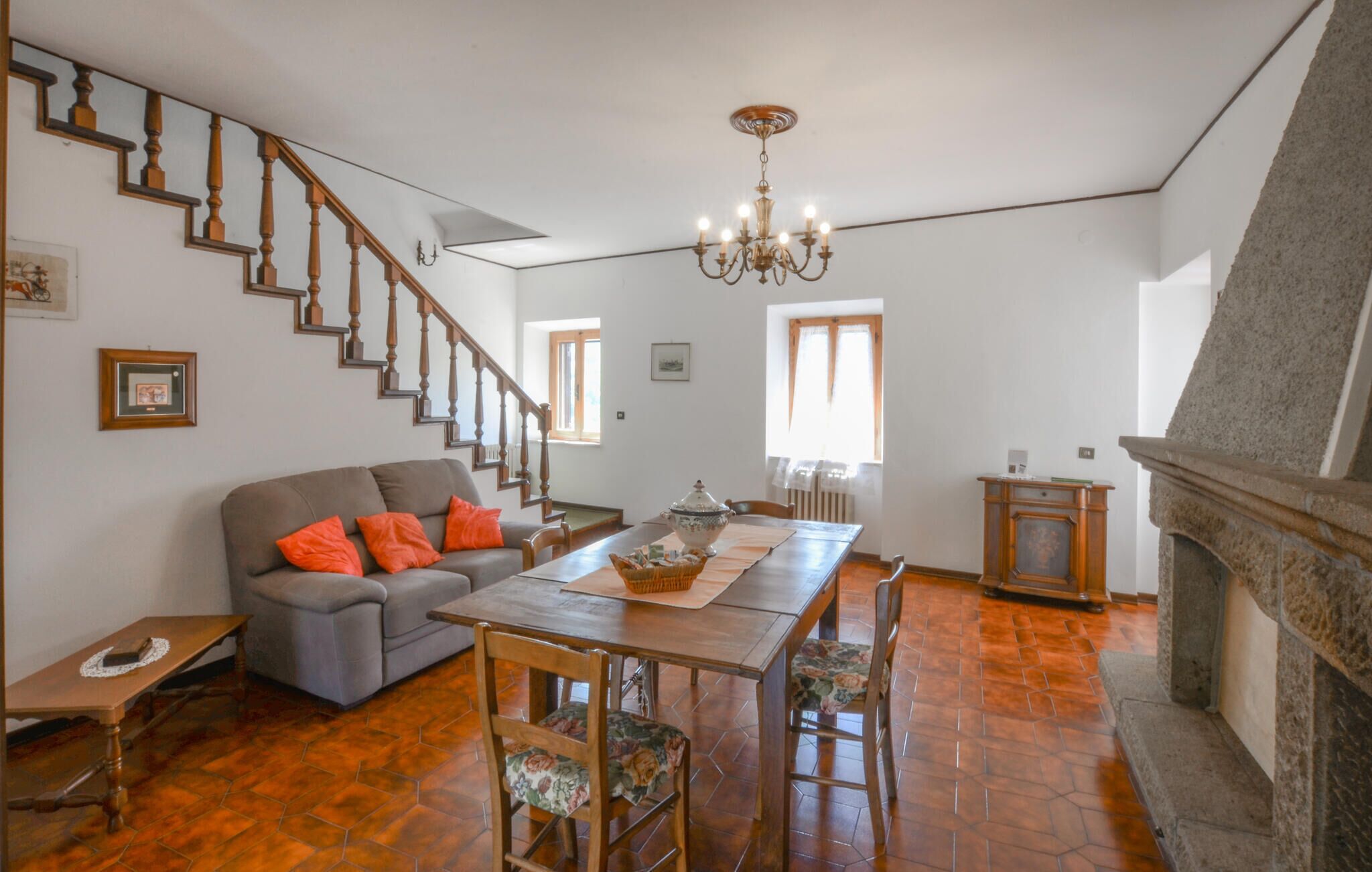 A spacious living room with a staircase, a dining table with chairs, a fireplace, and a chandelier.
