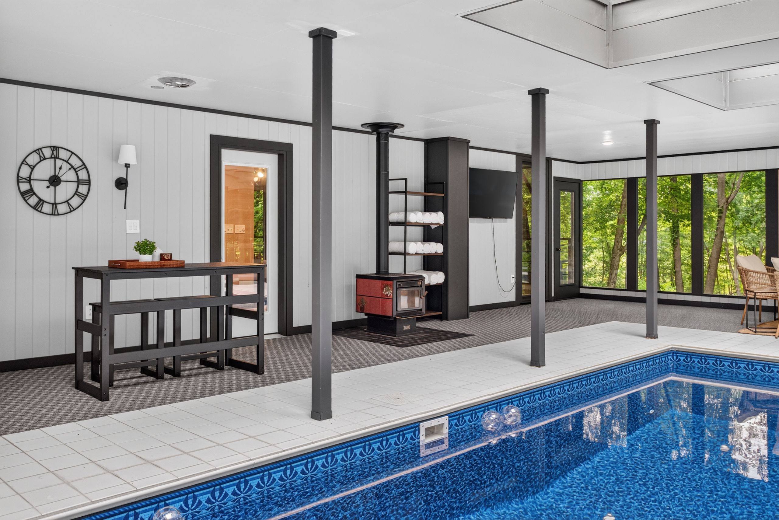 A modern indoor pool with a tiled floor, a built-in seating area, and a large window offering a view of greenery.