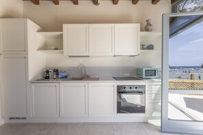 Eine Küche mit weißen Schränken, einem eingebauten Backofen und Meerblick durch eine Glastür.