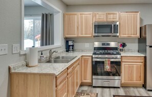 A modern kitchen with wooden cabinets, stainless steel appliances, a granite countertop, and a window with curtains. - Beautiful 2-bedroom cabin in charming Soldotna. Perfect for relaxing stays (Kasilof)
