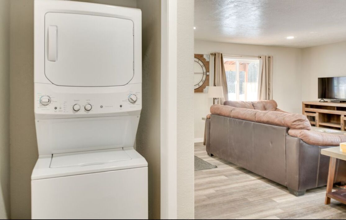 A white washing machine and a living room with a sofa, TV, and wooden furniture.
