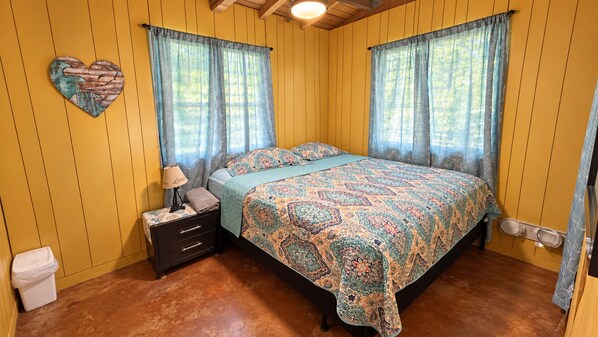 A bedroom with a bed, a nightstand, a wall-mounted heart decoration, and a window with curtains.