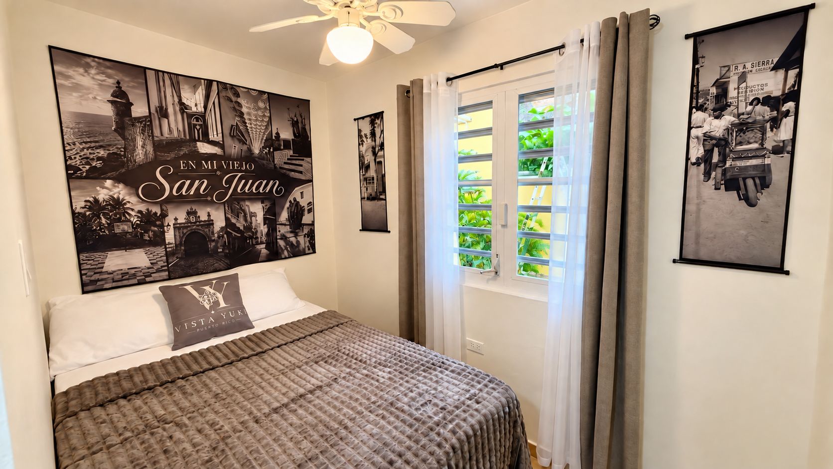 A bedroom with a bed, a ceiling fan, and two framed pictures on the wall.