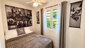 Un dormitorio con una cama, un ventilador de techo y dos cuadros en la pared.