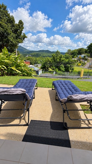 Two outdoor lounge chairs with a view of a green landscape and mountains in the distance.