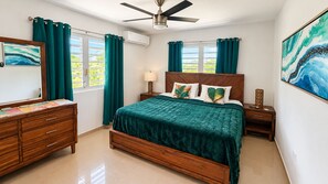 A bedroom with a bed, a dresser, a nightstand, a ceiling fan, and a window with curtains. - Vista YuKé ~ 7BR Mountain Escape ~ Saltwater Spa ~ Near El Yunque (Río)