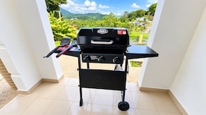 Ein tragbarer Grill mit Griff und Rädern, auf einem Fliesenboden platziert.