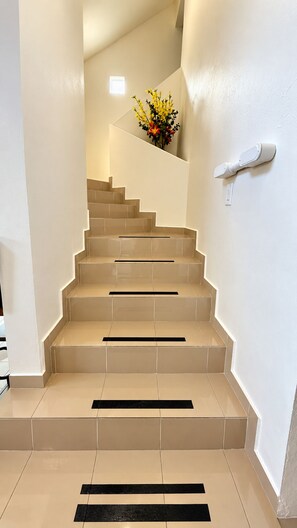 Una escalera con baldosas color crema y peldaños negros, que conduce a un rellano con un pequeño arreglo floral.