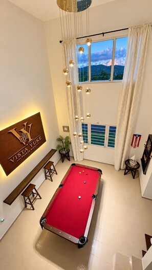 A pool table in a room with a view of a mountainous landscape through large windows, a wooden sign with the name 'Vista Yuke Puerto Rico', and a hanging light fixture. - Vista YuKé ~ 7BR Mountain Escape ~ Saltwater Spa ~ Near El Yunque (Río)