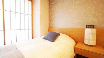 Quarto com cama, mesa de cabeceira, relógio de parede e janela com padrão de grade.