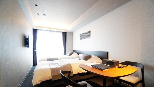 Habitación de hotel con cama, escritorio con silla, televisión en la pared y ventana con cortinas.
