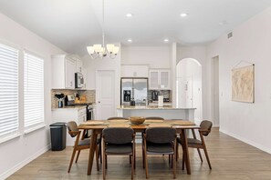 A modern kitchen with white cabinets, a central island, and a dining area with a wooden table and chairs.