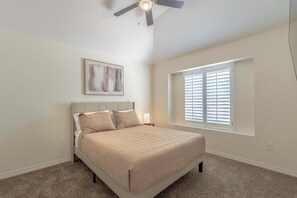 Ein Schlafzimmer mit Bett, Deckenventilator, Fenster mit Jalousien und einem Bild an der Wand.