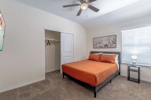 A bedroom with a bed, a ceiling fan, a closet, a window with blinds, and a painting on the wall.