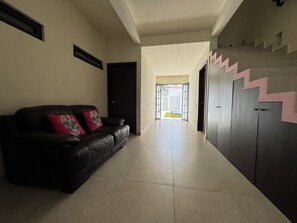 A hallway with a black leather sofa, a door, and a staircase with a zigzag pattern. - Rosa & Cioccolato (Cozumel)