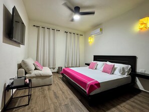 A hotel room with a bed, a sofa, a ceiling fan, an air conditioning unit, and a TV mounted on the wall. - Rosa & Cioccolato (Cozumel)
