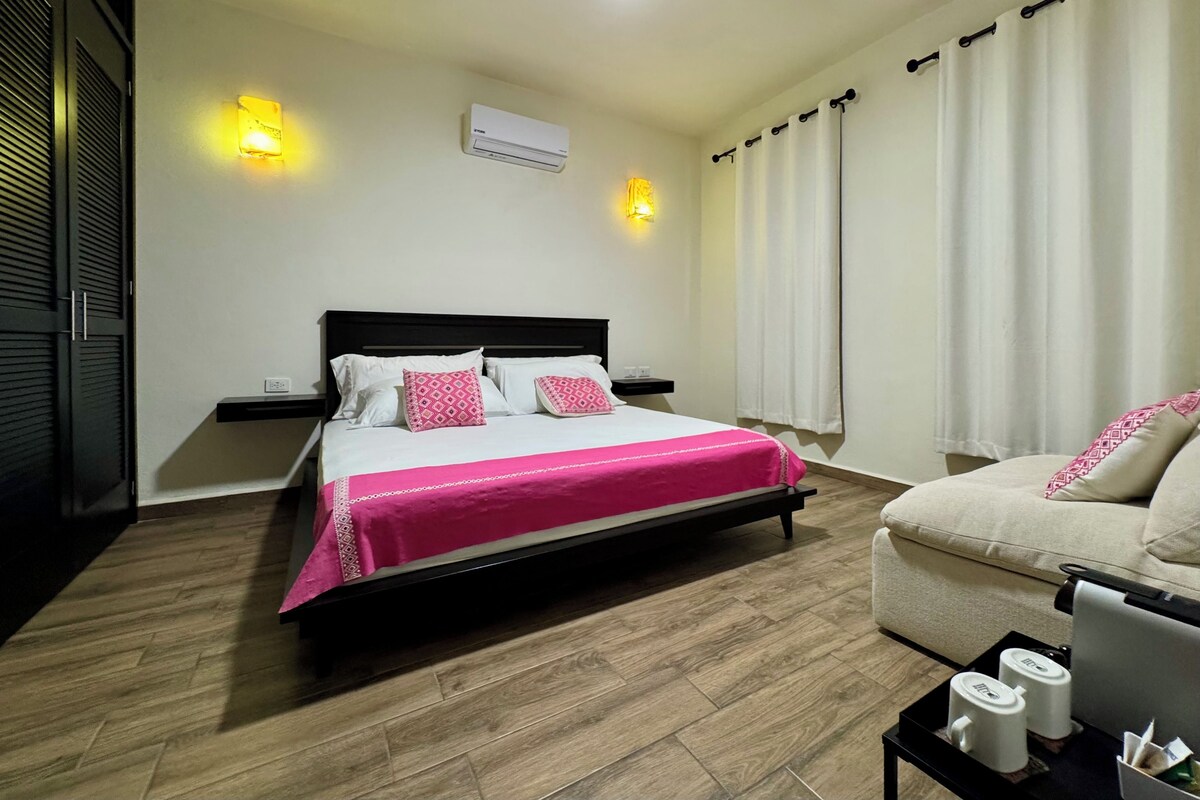 A bedroom with a bed, bedside table, nightstand, and a chair.