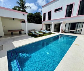 A swimming pool with lounge chairs and a bench, surrounded by a building with large windows and a white exterior. - Rosa & Cioccolato (Cozumel)