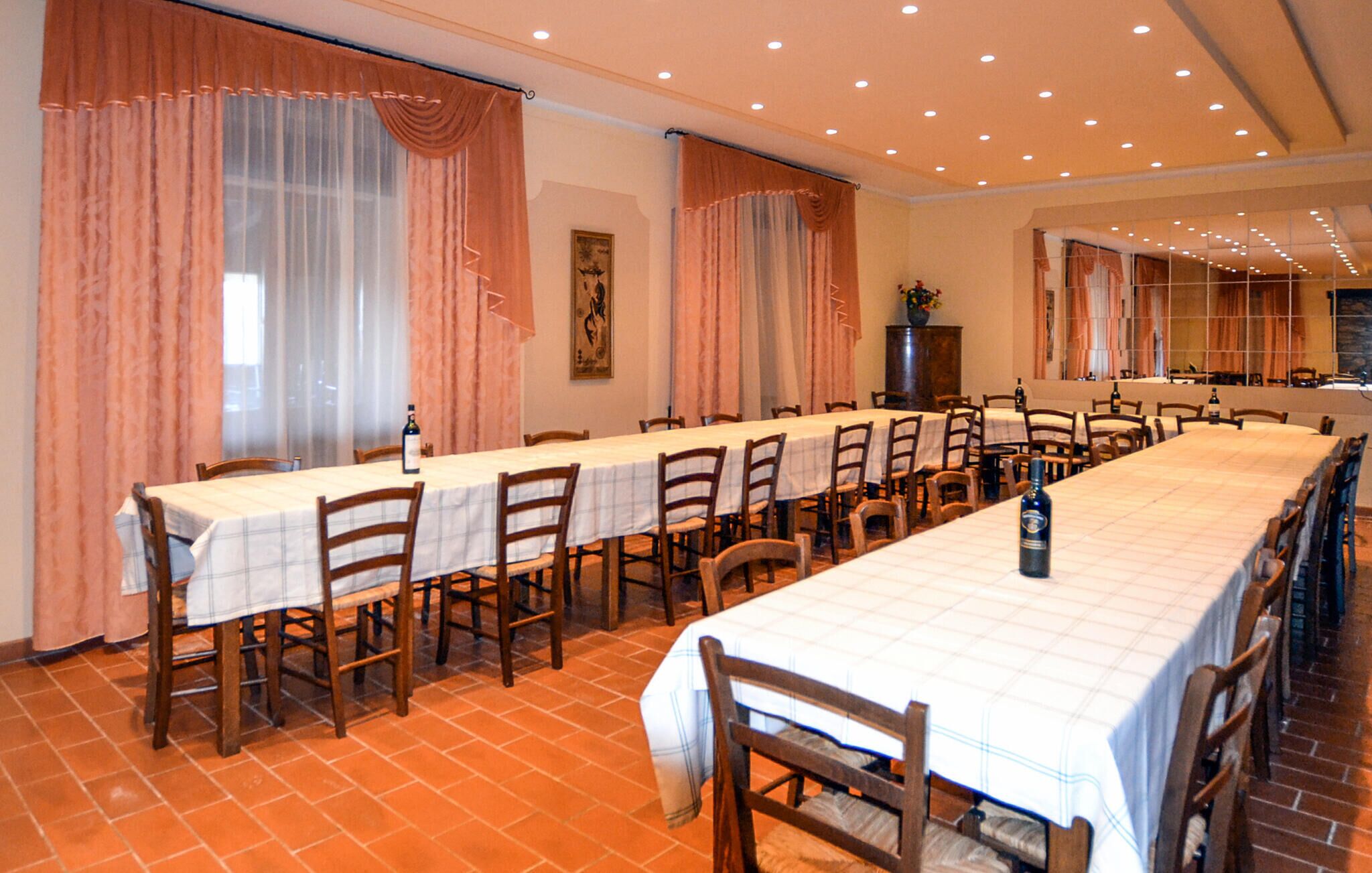 A long dining table with chairs, large windows with curtains, and a tiled floor.