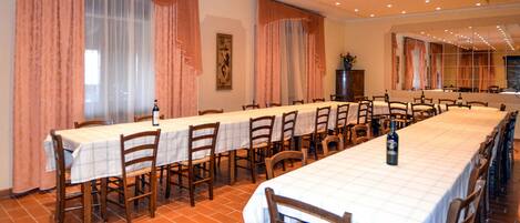A long dining table with chairs, large windows with curtains, and a tiled floor.