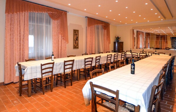 Una larga mesa de comedor con sillas, ventanas amplias con cortinas y un suelo de baldosas.