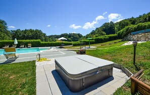Una piscina con sillones de descanso, un jacuzzi y una pared de piedra al fondo.