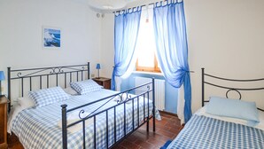 A bedroom with a double bed, a smaller single bed, a nightstand, a lamp, a window with blue curtains, and a wall-mounted light fixture. - Amazing home in Badia Tedalda (Badia Tedalda)