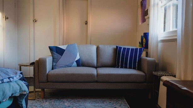 A neutral-colored sofa with patterned cushions, a patterned rug, and a small side table with a decorative item. - The Garden Flat - Charming Studio (Orange)