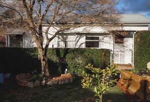 Ein Wohnhaus mit weißer Fassade, ein Baum im Vorgarten und ein gepflegter Garten mit verschiedenen Pflanzen und einem Holzzaun.