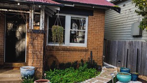 A brick house with a red roof, a hanging flower basket, and a garden with potted plants and a gravel pathway. - The Garden Flat - Charming Studio (Orange)
