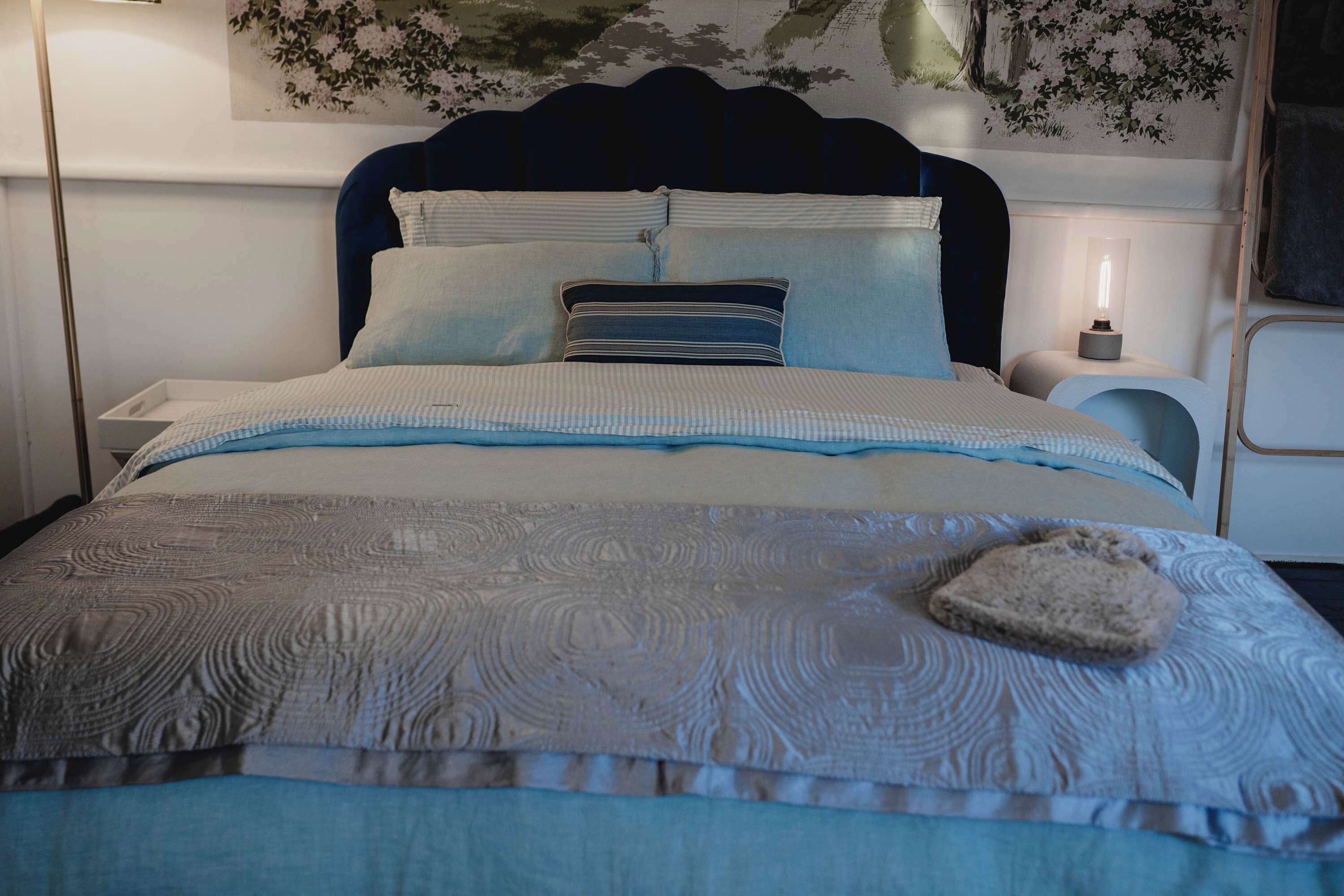 A neatly made bed with a patterned bedspread, pillows, and a bedside lamp.