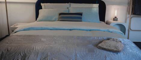 A neatly made bed with a patterned bedspread, pillows, and a bedside lamp.