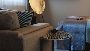 A room with a sofa, a small round table, a bed, a television mounted on the wall, and a patterned rug. - The Garden Flat - Charming Studio (Orange)