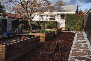 A garden with raised beds, a stone pathway, and a house in the background. - The Garden Flat - Charming Studio (Orange)