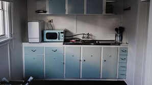 A compact kitchen with a microwave, a sink, and cabinets. - The Garden Flat - Charming Studio (Orange)
