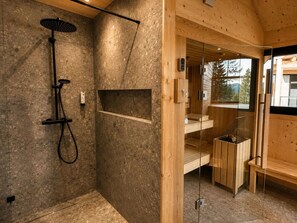 A modern bathroom with a shower, a glass-enclosed sauna, and a wooden interior. - 02_NTH050_18a_Sup Chalet mit Sauna und Hot Tub 2 E by Interhome (Großveitsch)