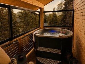 A hot tub with two glasses of red wine on a wooden deck with a view of trees and mountains. - 02_NTH050_18a_Sup Chalet mit Sauna und Hot Tub 2 E by Interhome (Großveitsch)