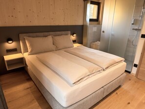 A modern bedroom with a large bed, nightstands, a window, and a shower area. - 02_NTH055_18f_Sup Chalet mit Sauna und Hot Tub 2 E by Interhome (Großveitsch)