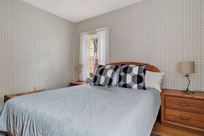 A bedroom with a bed, two nightstands, a window with curtains, and a wall with a checkered pattern.