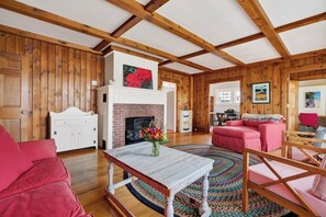 A room with wooden walls, a fireplace, a dining area, and a living room with a sofa and a table.