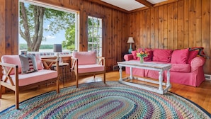 Una habitación acogedora con paredes de madera, un sofá rosa, un sillón a juego, una mesita pequeña y una alfombra colorida.
