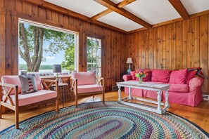 A cozy room with wooden walls, a pink sofa, a matching chair, a small table, and a colorful rug.