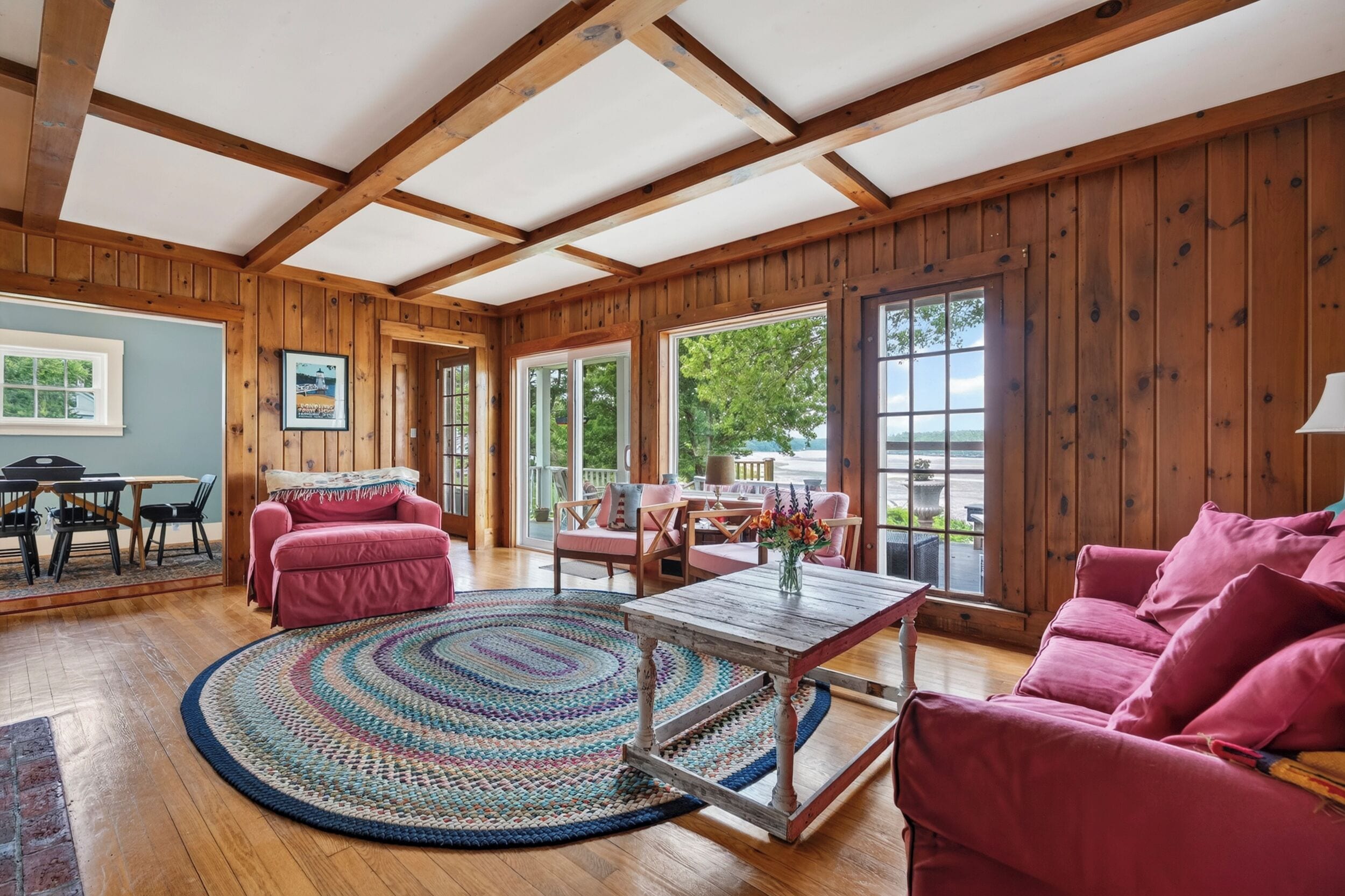 A cozy room with wooden walls, a large window, a round rug, and a wooden table.
