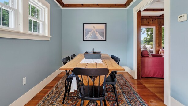 Un comedor con una mesa y sillas de madera, un cuadro en la pared y vistas al exterior a través de una ventana.