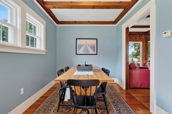 A dining area with a wooden table and chairs, a framed picture on the wall, and a view of the outdoors through a window.